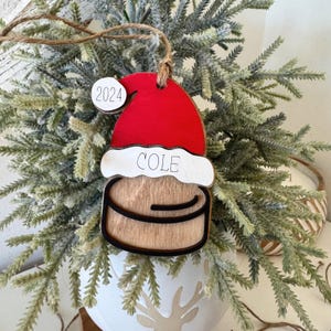 May include: Wooden Christmas ornament shaped like a Santa hat with the name "COLE" and the year "2024" on it.