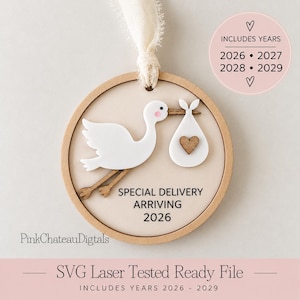 Op de afbeelding: Een rond houten ornament met een witte ooievaar die een bundel met een klein houten hartje draagt. De tekst luidt SPECIAL DELIVERY ARRIVING 2026. Een crèmekleurig lint is aan de bovenkant bevestigd. Een cirkelvormig inzetstuk vermeldt INCLUDES YEARS 2026 2027 2028 2029.