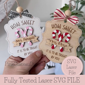 May include: Wooden teacher appreciation ornaments with candy cane designs. One ornament is white with pink candy canes and the name "Mrs. Pahapill". The other is natural wood with red candy canes and the name "Ms. Rose". Both say "How Sweet It Is To Be Taught By You".