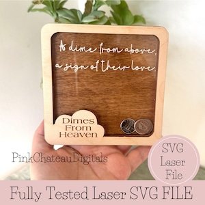 Könnte beinhalten: Holz-Schattenbox mit dunklem Holzmaserungshintergrund und hellem Holzrahmen. Die Box trägt den Schriftzug "A dime from above, a sign of their love" in weißer Schrift. Ein wolkenförmiger Ausschnitt zeigt "Dimes From Heaven". Zwei Münzen sind sichtbar.