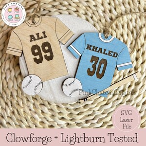 Puede incluir: Dos adornos de camiseta de b&eacute;isbol de madera con pelotas de b&eacute;isbol y un bate. Las camisetas son beige y azul claro con los nombres "ALI 99" y "KHALED 30" en ellas.