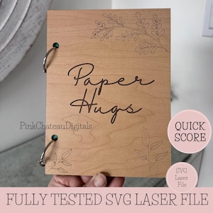May include: A light-colored wooden notebook with the words "Paper Hugs" in cursive. The notebook has a floral design etched into the wood. The text "PinkChateauDigitals" is also visible. The bottom of the image reads "FULLY TESTED SVG LASER FILE".
