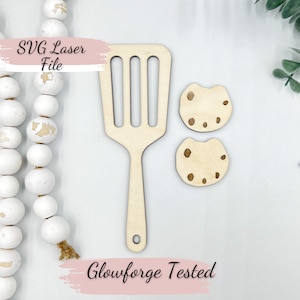 Puede incluir: Una espátula de madera con ranuras y dos recortes de galletas de madera con manchas marrones. El texto "SVG Laser File" y "Glowforge Tested" se muestra en la imagen.