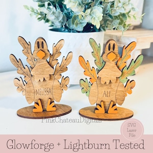 May include: Two wooden turkey place card holders with fall leaves and the names "Melissa" and "Ali" written on them. The turkeys are standing on a wooden base. The image is labeled "Glowforge + Lightburn Tested" and "SVG Laser File".
