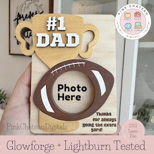 Op de afbeelding: Een houten trofee met een voetbalontwerp en een fotolijst. De trofee zegt "#1 DAD" en "Photo Here". De tekst "Thanks for always going the extra yard!" staat ook op de trofee. De trofee staat op een houten achtergrond.