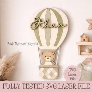 May include: A wooden hot air balloon wall decor piece with the name "Ethan" in script. The balloon is cream and green, with a teddy bear in the basket. The text "FULLY TESTED SVG LASER FILE" is at the bottom.