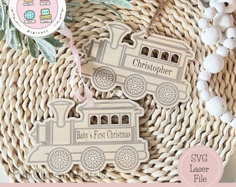 May include: Two wooden train ornaments, one with the text "Baby's First Christmas" and the other with the name "Christopher". The ornaments are on a woven background with white beads.