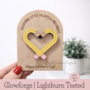 May include: A wooden Valentine's Day card with a heart-shaped pencil design. The pencils are yellow with pink erasers and a black tip. The card reads "Teaching Little Hearts & Big Minds" and "Happy Valentine's Day!"