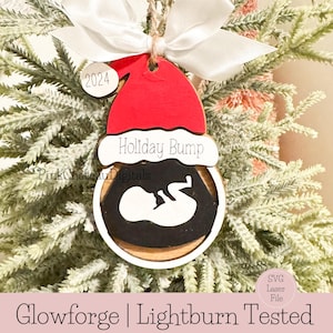 May include: A wooden Christmas bauble featuring a red Santa hat, a black and white silhouette of a baby within a circle, and the text "Holiday Bump" on the hat. The bauble also has a small tag with the year "2024" on it.