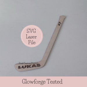 Könnte beinhalten: Ein Holzhockeyschläger mit dem Namen "Lukas" und der Nummer "#7" eingraviert. Der Schläger befindet sich auf einem weißen Hintergrund mit dem Text "SVG Laser File" und "Glowforge Tested" in einem Kreis und am unteren Rand des Bildes.