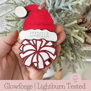 May include: Red and white wooden Christmas bauble shaped like a Santa hat with a pom-pom on top. The bauble has the name "ISABELLA" written on it.