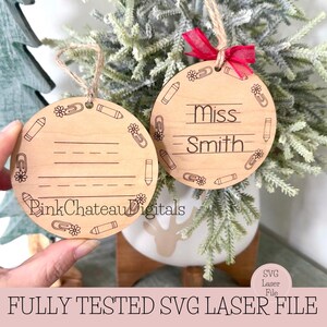 Puede incluir: Dos adornos de madera para el agradecimiento a los profesores. Un adorno tiene grabado el nombre "Miss Smith". Ambos adornos tienen un diseño de lápiz, flor y clip alrededor de los bordes. Los adornos cuelgan de una cuerda y una cinta roja.