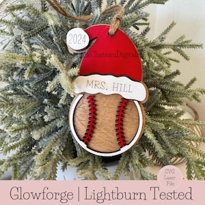 May include: A wooden Christmas bauble shaped like a baseball with a Santa hat on top. The bauble is red, white and brown. The hat has the text "MRS. HILL" on it. The bauble also has a small white circle with the text "2024" on it.