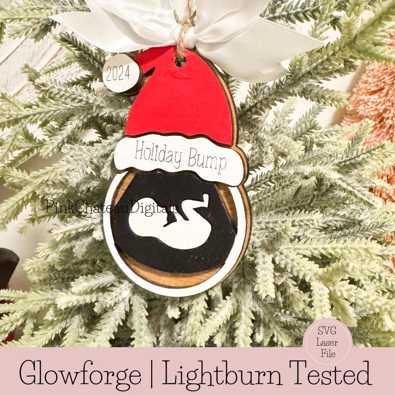 May include: A wooden Christmas bauble featuring a red Santa hat and the text "Holiday Bump". The bauble is decorated with a white silhouette of a baby inside a black circle. The bauble is hanging on a green Christmas tree.