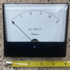 May include: A black and white analog DC volt meter with a black needle pointing to the 10 volt mark. The meter is labeled "DC VOLTS" and "Simpson".