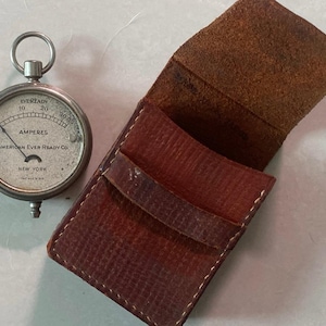 May include: A silver pocket-sized ammeter with a leather case. The ammeter face reads "Eveready" and "American Ever Ready Co. New York".