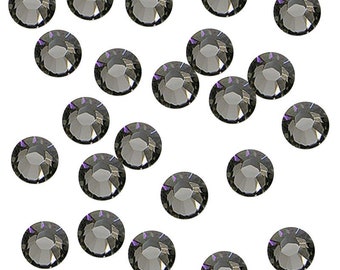 May include: A scattering of black rhinestones on a white background. The rhinestones are round and have a faceted surface.