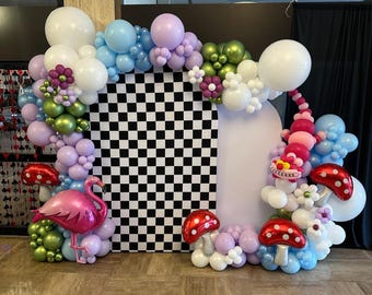 May include: A whimsical balloon arch featuring a black and white checkered backdrop, adorned with pink flamingo, mushroom, and caterpillar balloons. The arch includes white, blue, green, and purple balloons, creating a vibrant and playful display, perfect for a party.