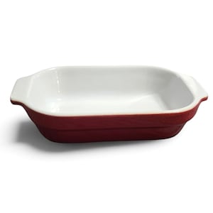May include: A rectangular baking dish with a glossy white interior and a deep red exterior. The dish features integrated handles on both short ends and has a smooth, curved rim design, providing a functional vessel for oven-based food preparation.