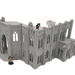 Peut inclure: Un bâtiment miniature de style gothique gris avec des fenêtres cintrées et des détails de maçonnerie. Deux figurines miniatures sont positionnées sur la structure. Le bâtiment semble être un modèle pour les jeux de société ou un passe-temps similaire.