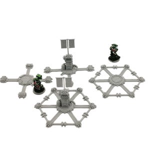 May include: A selection of grey miniature terrain pieces for tabletop gaming. The set includes platforms, towers with flags, and hexagonal structures. Miniature figures with green and red accents are also present, suggesting a war game setting.