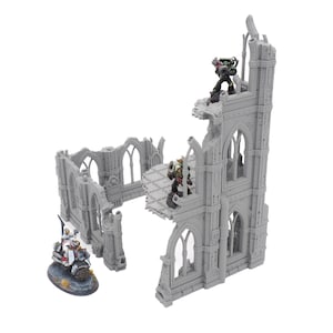 May include: A gray miniature model of a ruined gothic building with arched windows and battle figures. The model has a detailed, weathered appearance, with figures positioned on the structure.