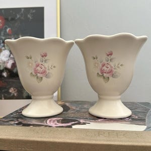May include: A set of three ceramic mugs with a speckled, cream-colored glaze. Each mug features a different hand-painted floral design in shades of blue, green, and yellow. The mugs have a simple, rounded shape and a comfortable handle.