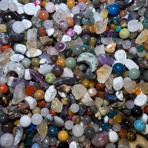 May include: A collection of various polished gemstones and crystals in a variety of shapes and sizes. The gemstones are in shades of blue, green, orange, purple, and clear. Some are spherical, while others are irregular or faceted.