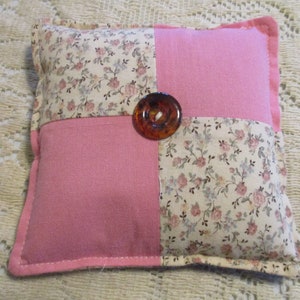 Puede incluir: Una almohada rosa con estampado floral y un botón marrón en el centro.