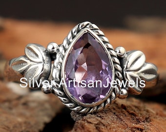 May include: A sterling silver ring featuring a pear-shaped, light purple amethyst gemstone. The ring has a detailed, ornate design with leaf accents on the sides and a twisted rope-like border around the gemstone. The text "Silver Artisan Jewels" is visible.