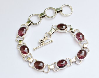 May include: A silver bracelet with a toggle clasp and oval-shaped purple gemstones.