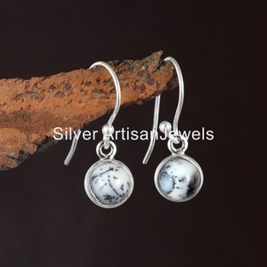 May include: A pair of silver dangle earrings featuring white and black dendritic opal stones. The earrings are suspended from a wooden branch.