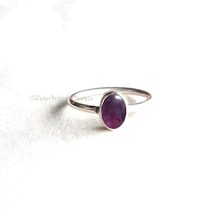 Könnte beinhalten: Ein silberner Ring mit einem violetten ovalen Edelstein.