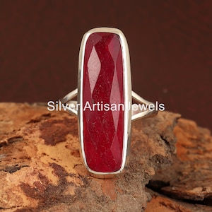 May include: A silver ring featuring a large, rectangular, red gemstone. The gemstone has a faceted cut and is set in a simple, silver band.