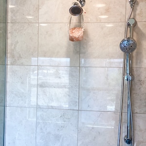 May include: A chrome shower head with a handheld sprayer and a pink Himalayan salt soap on a rope hanging from the shower head.