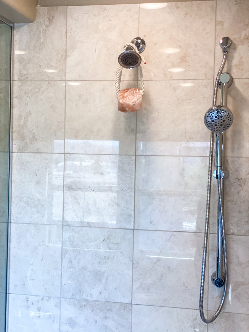 May include: A chrome shower head with a handheld sprayer and a pink Himalayan salt soap on a rope hanging from the shower head.