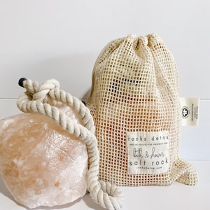 May include: A large pink Himalayan salt rock with a rope handle and a smaller pink Himalayan salt rock in a beige mesh bag. The bag has a label that reads "rocks detox 100% all natural Pink Himalayan Salt bath & shower salt rock rocksdetox.com".
