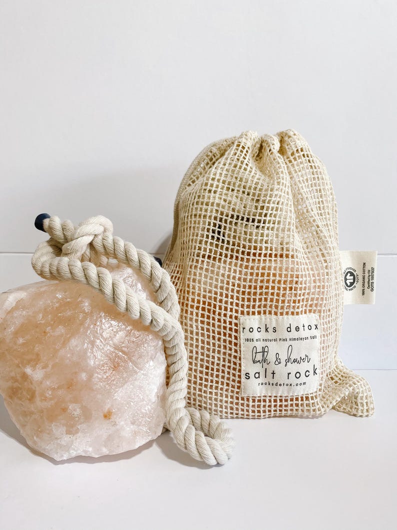 May include: A large pink Himalayan salt rock with a rope handle and a smaller pink Himalayan salt rock in a beige mesh bag. The bag has a label that reads "rocks detox 100% all natural Pink Himalayan Salt bath & shower salt rock rocksdetox.com".