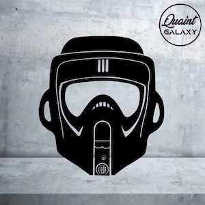 May include: Black graphic of a Scout Trooper helmet. The helmet features a visor, breathing apparatus, and three vertical lines on top. The image includes the text "Quaint Galaxy" in a circular design.