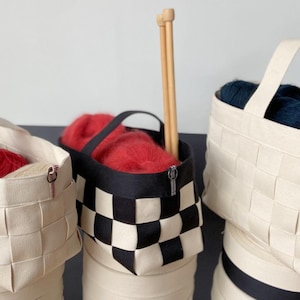 May include: Three woven canvas storage baskets with zipper closures. The baskets are filled with yarn in various colours, including red, blue, and pink. One basket has a black and white chequered pattern.