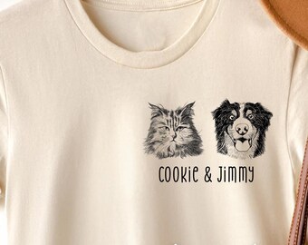 Puede incluir: Una camiseta blanca con una ilustración en blanco y negro de un gato y un perro. El texto "Cookie & Jimmy" está impreso debajo de las ilustraciones. Dos imágenes más pequeñas del gato y el perro se muestran debajo de la camiseta.
