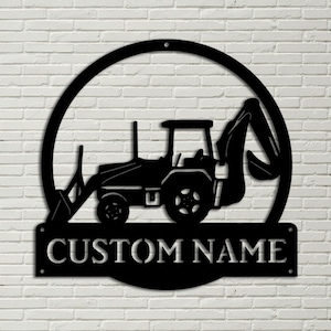 Puede incluir: Arte mural de silueta de tractor de metal negro con un marco circular y una placa con el nombre rectangular que dice "CUSTOM NAME". El tractor está montado en una pared de ladrillos blancos.