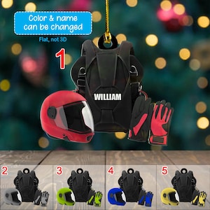 May include: A personalized ornament featuring a black parachute, a red helmet, and red and black gloves. The name "WILLIAM" is displayed on the parachute. The text "Color & name can be changed" is visible.