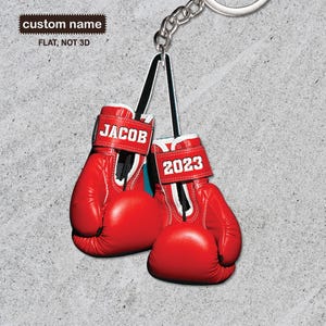 May include: Red boxing gloves keychain with the name "JACOB" and the year "2023" printed on them.