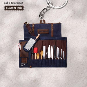 Peut inclure: Un rouleau à couteaux en toile bleu marine avec des détails en cuir marron et le nom "Jackson" sur un patch en cuir. Le rouleau contient divers couteaux de cuisine, ustensiles et une hachette. Un porte-clés est attaché en haut.