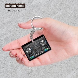 Puede incluir: Un llavero de mezclador de DJ negro y plateado con el nombre "JACOB" impreso en él.