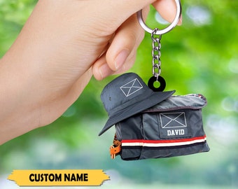 May include: A blue and gray mail carrier bag keychain with a matching blue hat. The bag has a white envelope with the word "DAVID" printed on it.