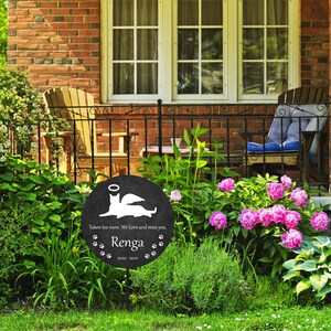 May include: Black memorial garden stake with a white silhouette of a cat with wings and a halo. The stake reads "Taken too soon. We love and miss you. Renga 2020-2022" with paw prints.