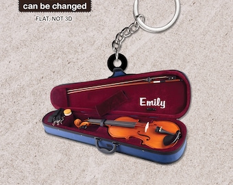Puede incluir: Un llavero de estuche de violín azul con un llavero plateado. El estuche está abierto y hay un violín dentro. El violín es marrón con un interior rojo. El estuche tiene el nombre "Emily" escrito en él.