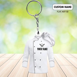 Puede incluir: Llavero de chaqueta de chef blanca con un gorro de chef negro, cuchillos cruzados y el texto "YOUR NAME".